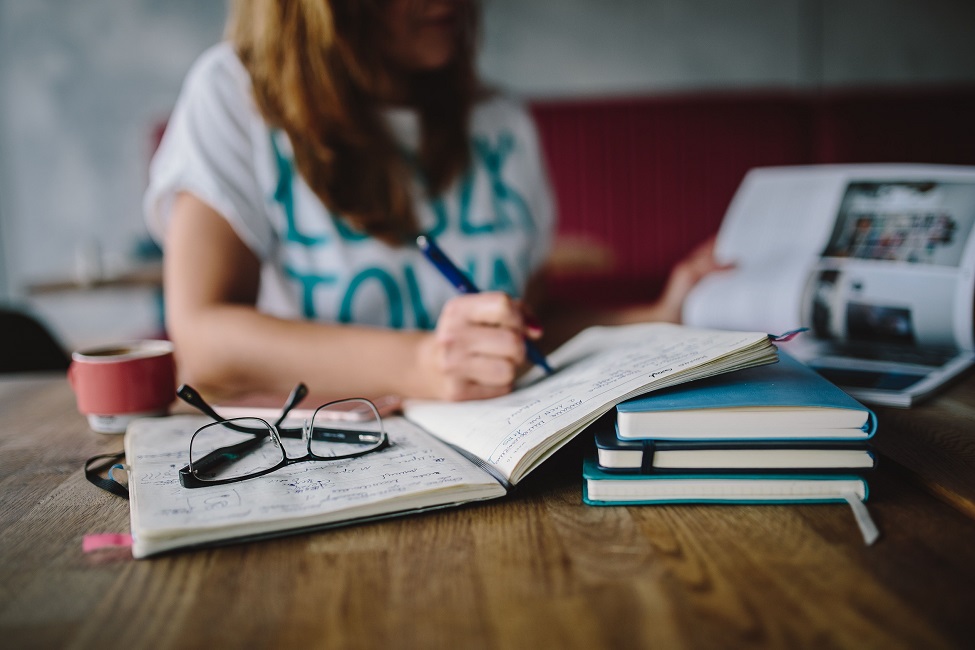 Μαθήτρια σε μελέτη με σημειώσεις, τετράδια και εστίαση στην προετοιμασία